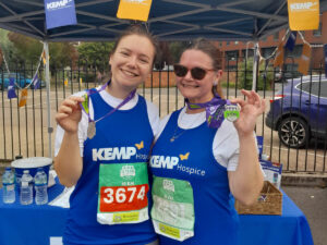 two women stand wearing blue running vests