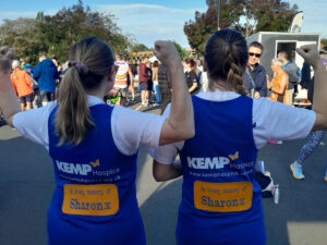 two people stand facing away form the camera with arms in the air wearing blue running vests