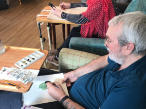 a man sits painting a bird in watercolors