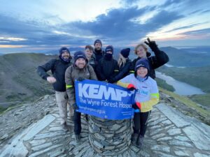 a group of people stand on top of snowdon mountain holding a kemp hospice sign