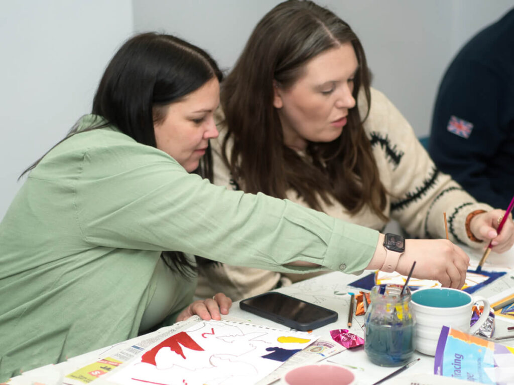 two ladies sit at a table completing creative therapy tasks