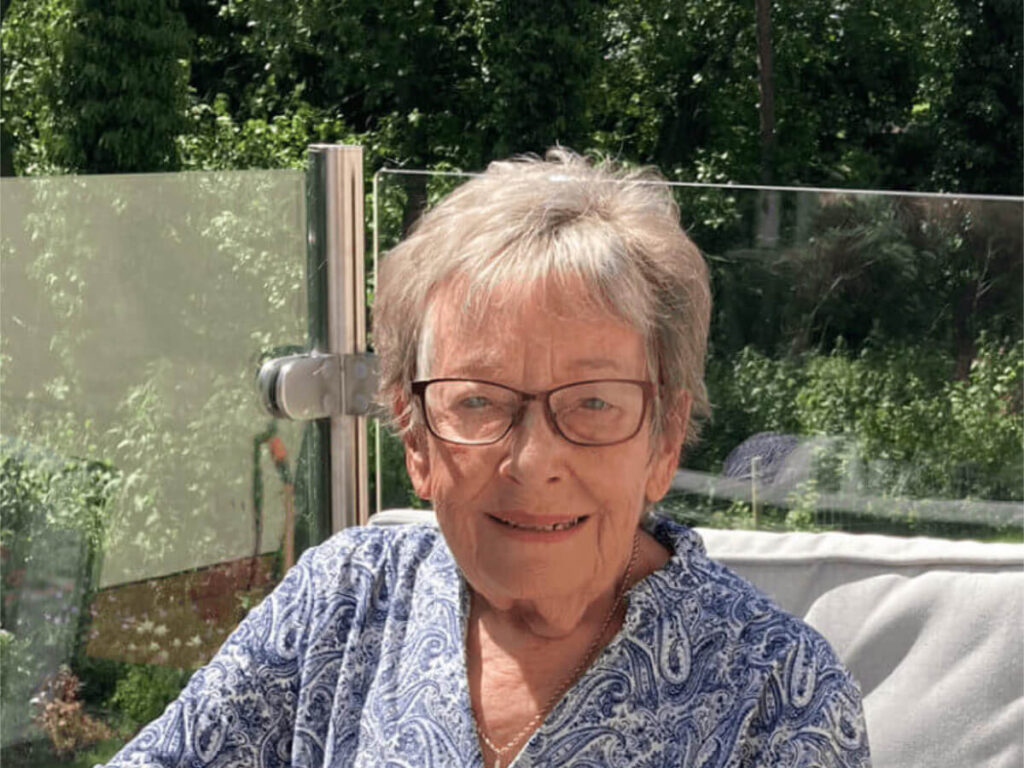 a lady sits in a sunny garden with trees in the background