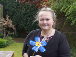 a lady stand in a garden holding a metal forget me not flower statue