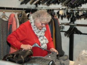 a lady stands sorting clothes. she wears a red top and cream scarf and puts an item of clothing on a clothes hangar
