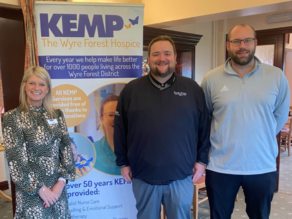 A lady stands next to a kemp banner with two gentlemen stood next to her.