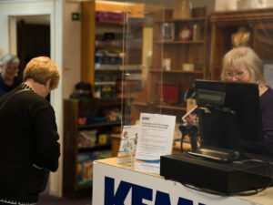 a lady stands behind a till while another lady purchases an item