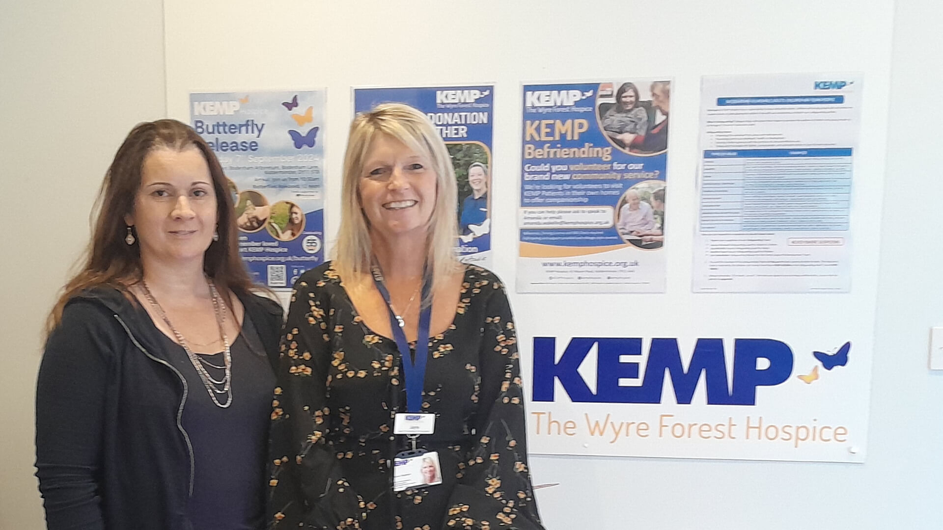two ladies stand by a white wall with a KEMP logo in the background