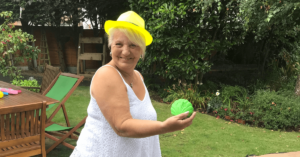a lady stands in a garden holding a tennis ball wearing a yellow hat