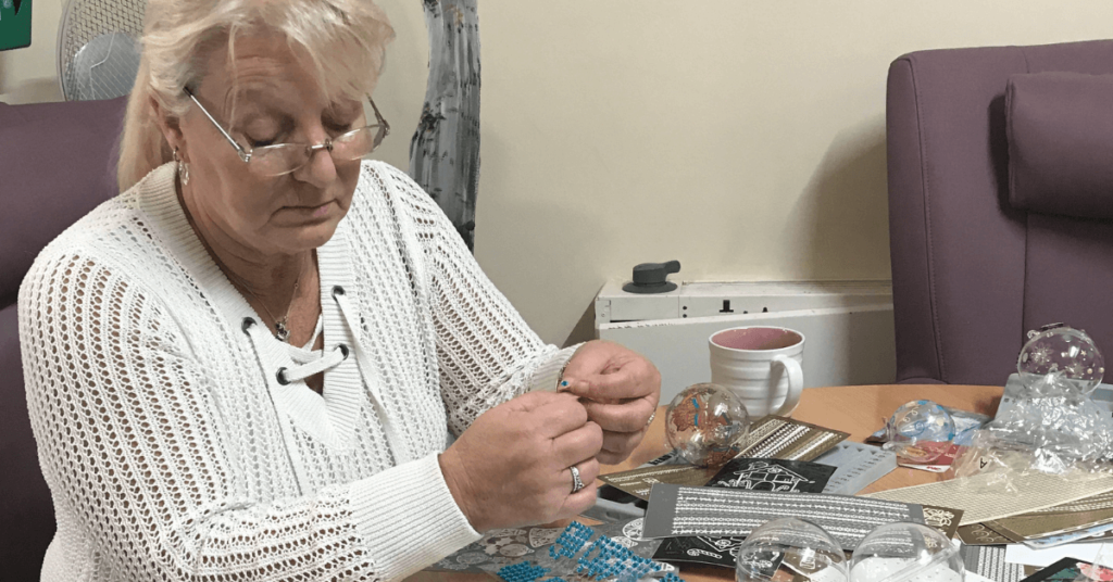 a lady sits at a table with craft materials in front of her
