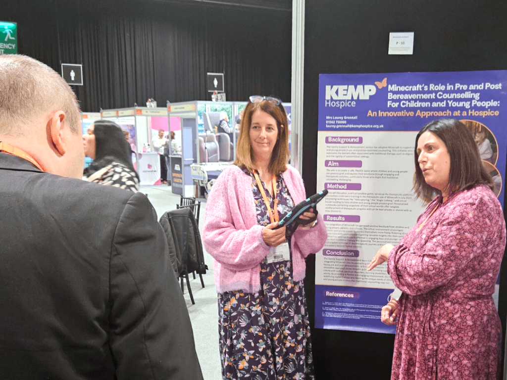 two people stand by a poster board whilst talking to another person in a suit