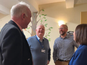 four people stand together inside a hospice activity room talking