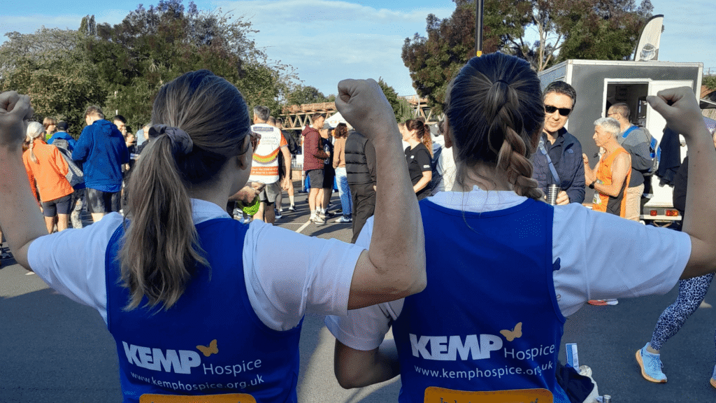 the back of two ladies wearing blue kemp running vests and holding their arms in a strong position