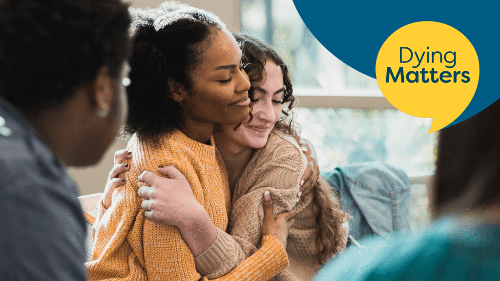 Yellow circle with back text to say Dying Matters at the top right. Two ladies sit hugging to the left of image. Both are smiling.