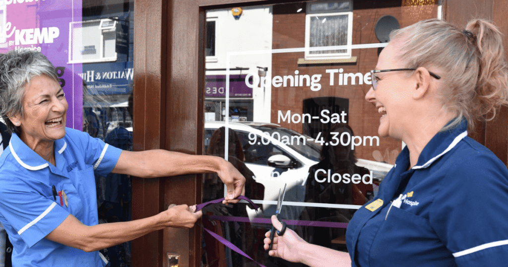 two ladies wearing KEMP nurse tops stand together smiling and cut a ribbon on a door