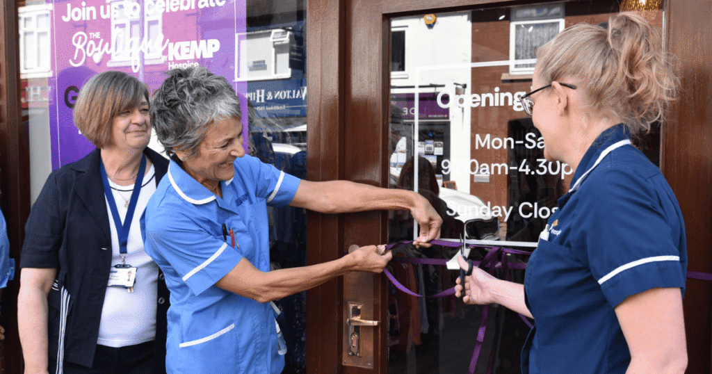 two ladies wearing KEMP nurse tops and another lady stand together and cut a ribbon on a door