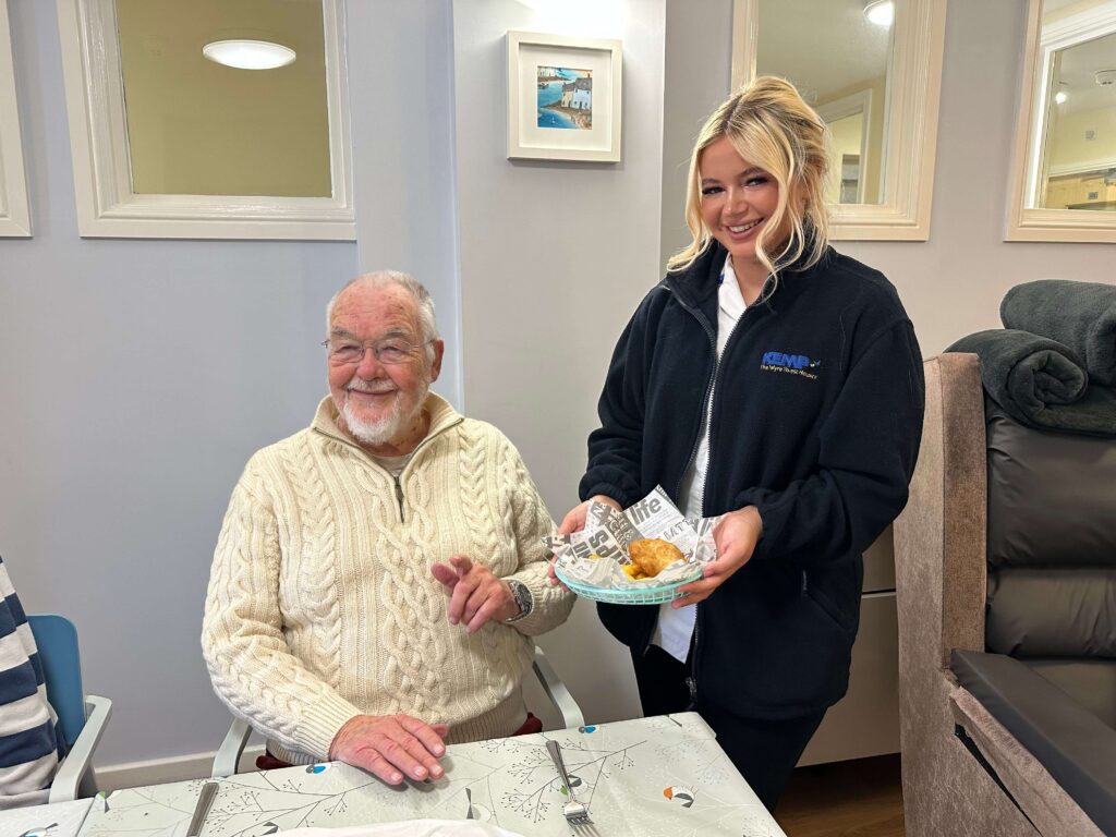 A nurse and a patient together smiling as she serves him fish and chips