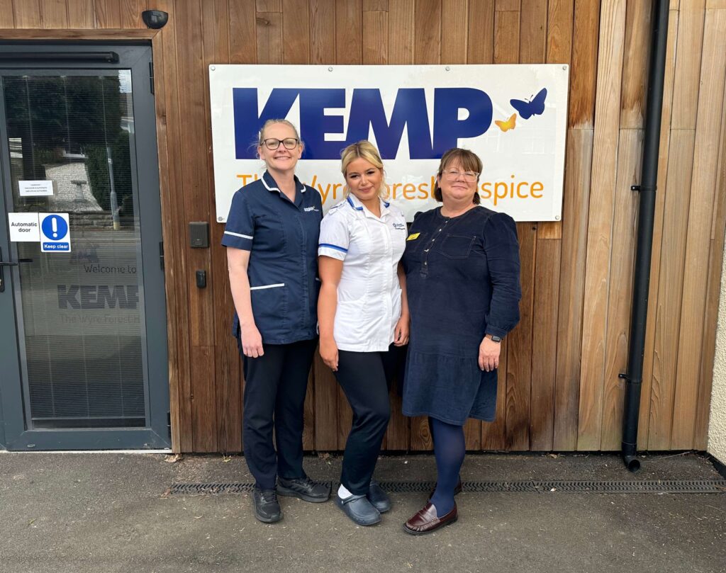 three nurses stood smiling in front of the KEMP Hospice sign
