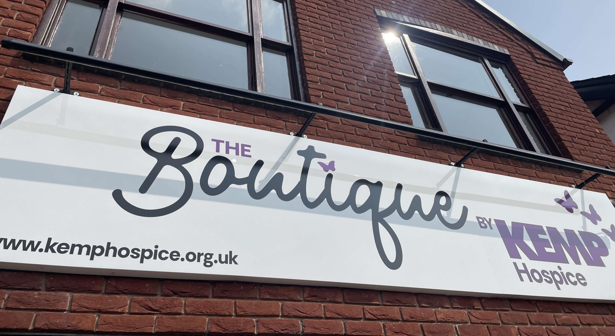 close up of boutique shop signage saying the boutique by kemp hospice. The sign is located on a brick building.