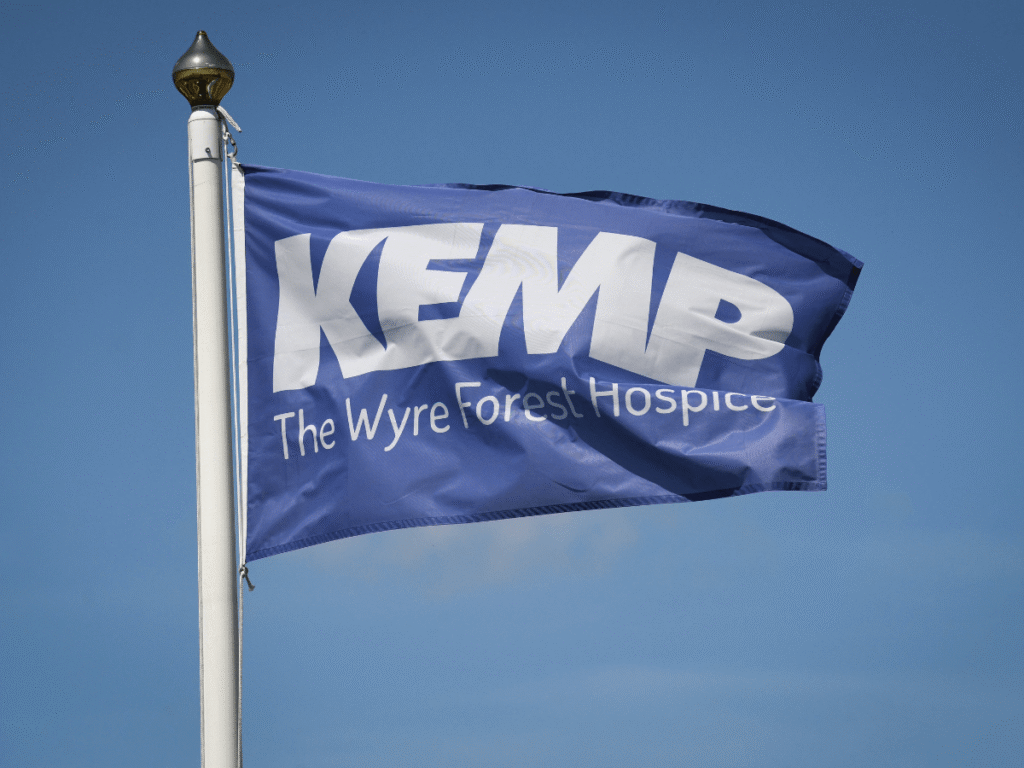 a blue flag blowing on a flag pole with the words kemp the wyre forest hospice in white text.