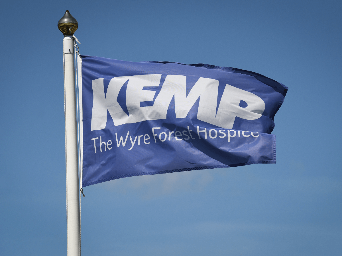 a blue flag blowing on a flag pole with the words kemp the wyre forest hospice in white text.