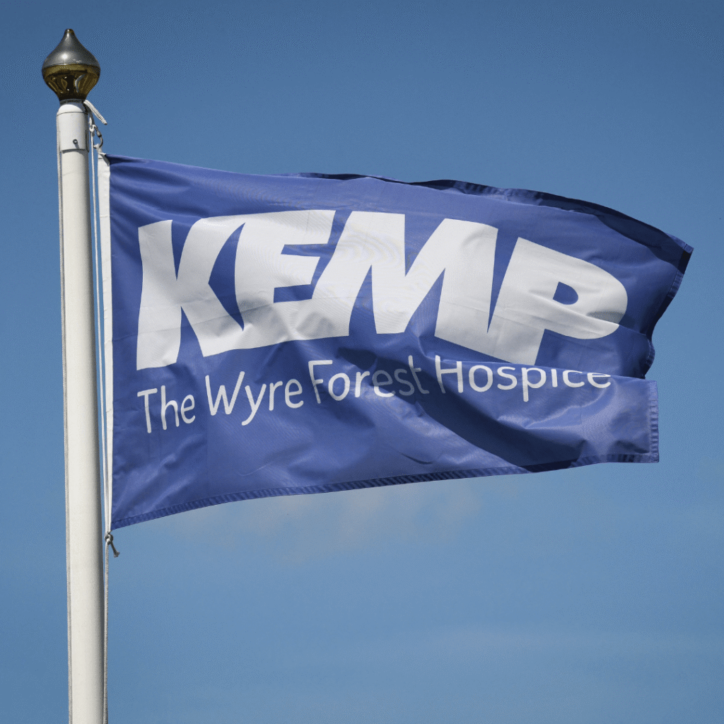 a blue flag blowing on a flag pole with the words kemp the wyre forest hospice in white text.