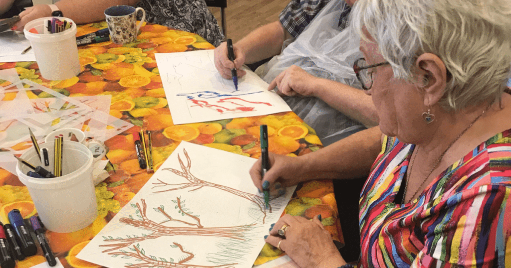 close up of a lady in a multi coloured top draws a picture of trees on a piece of paper.