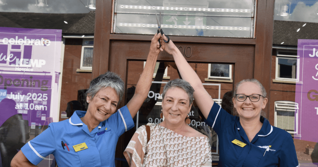two nurses hold scissors in the air stood with another lady who is about to enter the KEMP shop