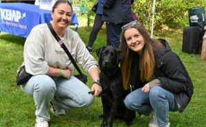 two people kneel down next to a dog with all looking at the camera