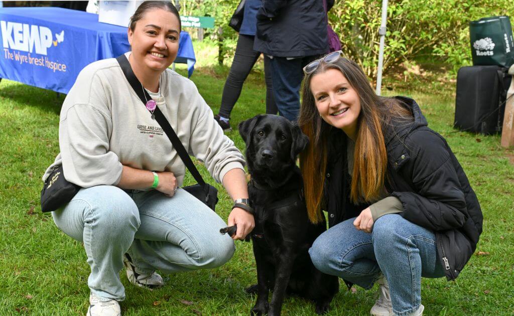 two people kneel down next to a dog with all looking at the camera