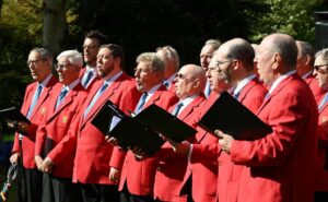 a group of male singers in red jackets singing at an outdoor event