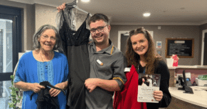 three people stand in a room holding clothing items