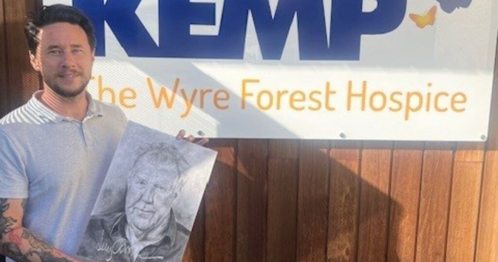 A gentleman stands next to a kemp hospice sign outside holding a hand drawn picture of Jeremy Clarkson.
