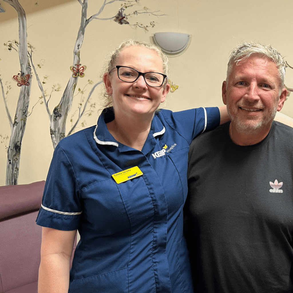 a man in a black t shirt stands on the right with a nurse stood on the left wit her arm around his shoulders.