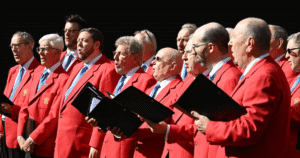 a group of male singers stand together wearing red jackets.