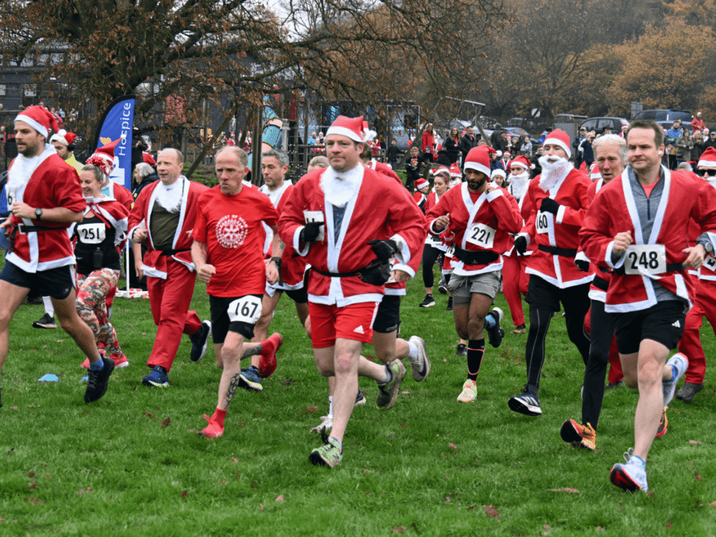 a group of people wearing santa suits running on grass at the kemp santa fun run