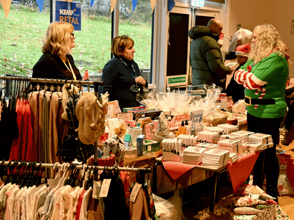 a table of retail items from kemp charity shops and three ladies standing talking to each other at the kemp santa fun run