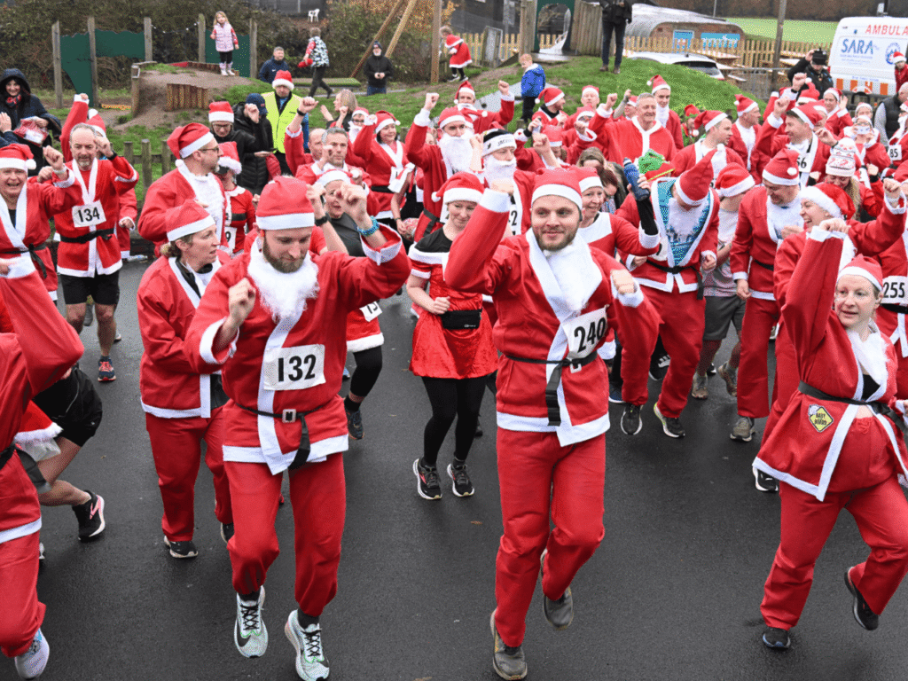 a group of people wearing santa suits doing an exercise warm up on tarmac at the kemp santa fun run