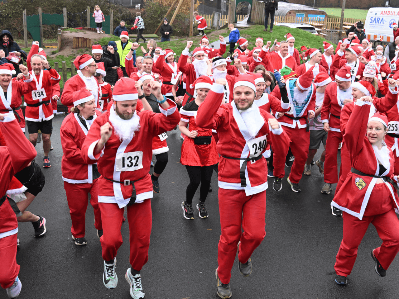 a group of people wearing santa suits doing an exercise warm up on tarmac at the kemp santa fun run