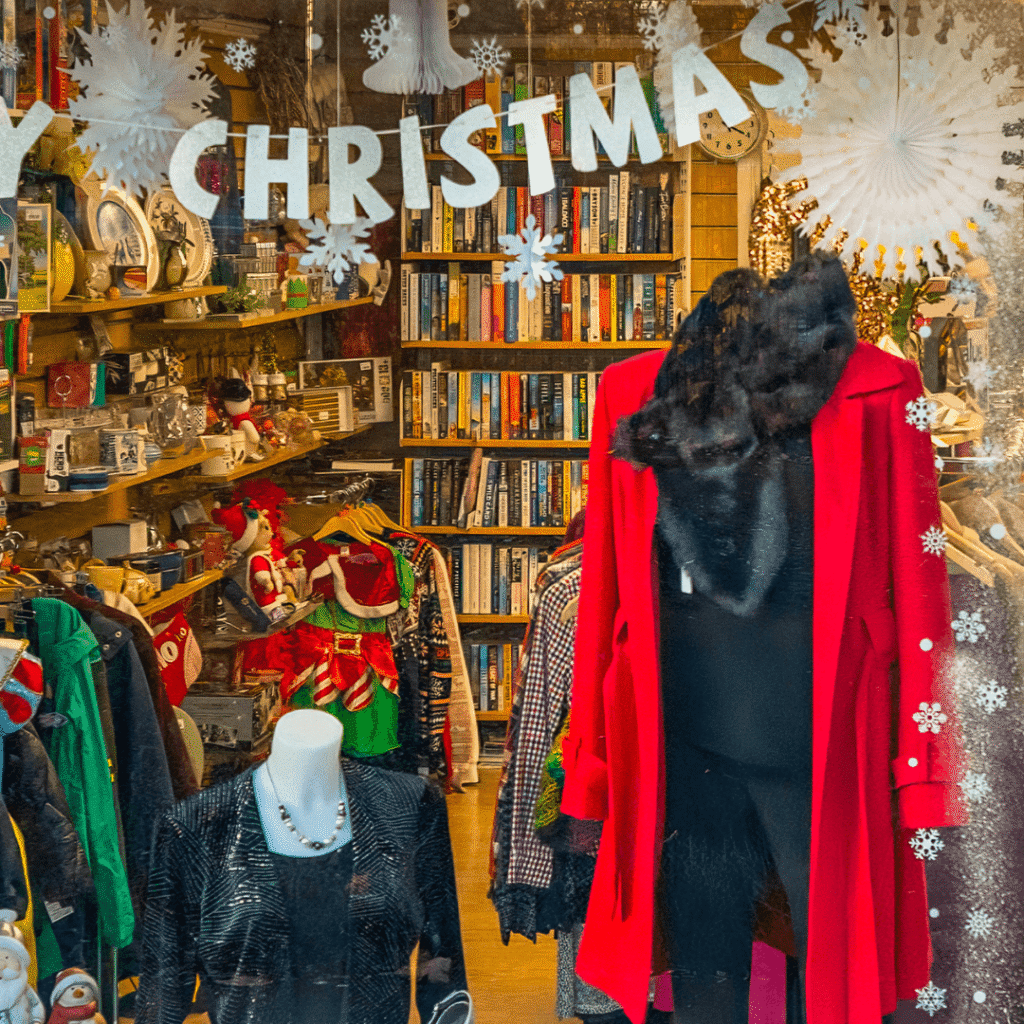a shop window display of a red jackets on a mannequin with a black dress underneath and a christmas banner hanging across the window.