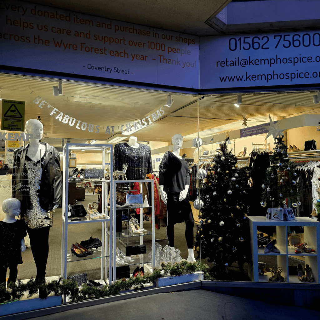 a nightnight photo of a shop window displaing christmas trees and a number of mannequins showing sparkly clothing.