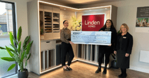 three ladies stand in a room with tile samples and a linden homes sign in the background. They are holding a large cheque made out to kemp hospice.