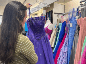 A lady with long brown hair wearing a striped top looks at a dark purple dress