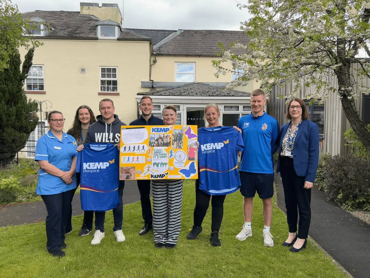 a group of people stand in the garden of kemp hospice holding banners and kemp t shirts