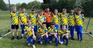 a groups of young people stand in a goal wearing football kits with KEMP Hospice sponsorship