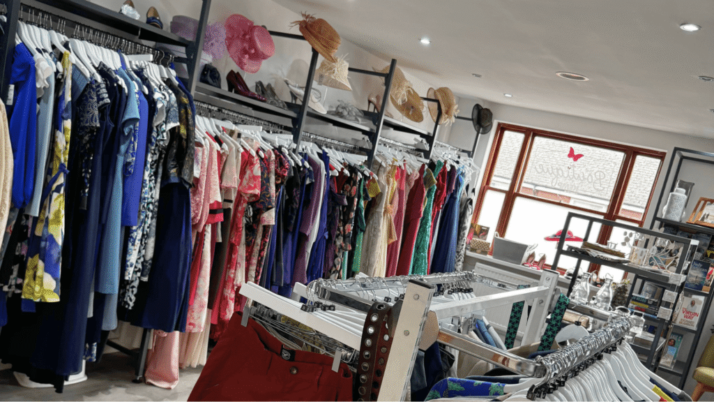 clothes rails arranged around a shop with soe books and a window in the background.
