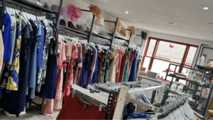 clothes rails arranged around a shop with soe books and a window in the background.