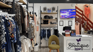 clothes rails with colourful ladies clothing, a shops till and a tv screen in the background