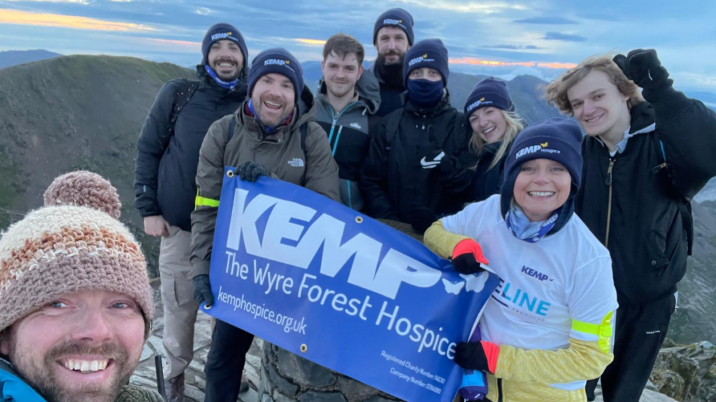 group of people smiling at the top of a summit at sunrise