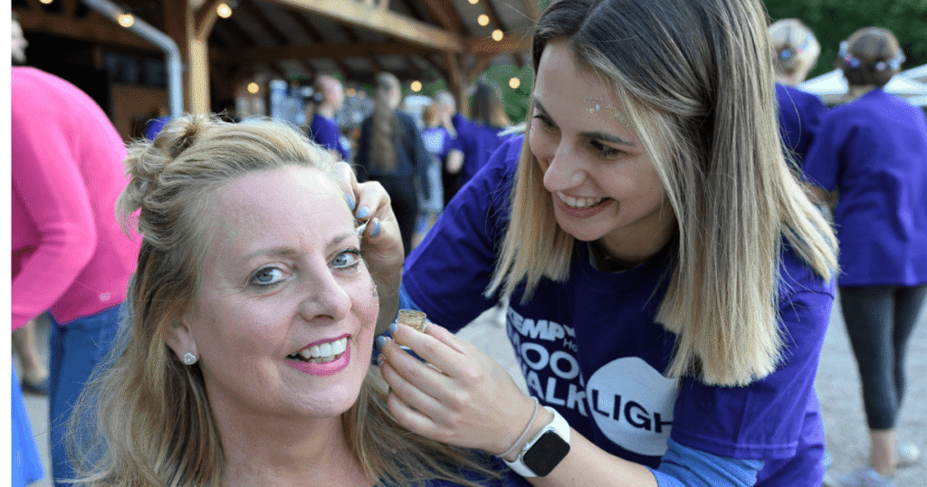 a lady sits having glitter painted to her face
