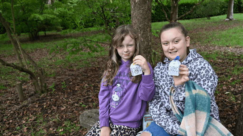 Two young ladies sit together holding a white decorative box with a butterfly inside.